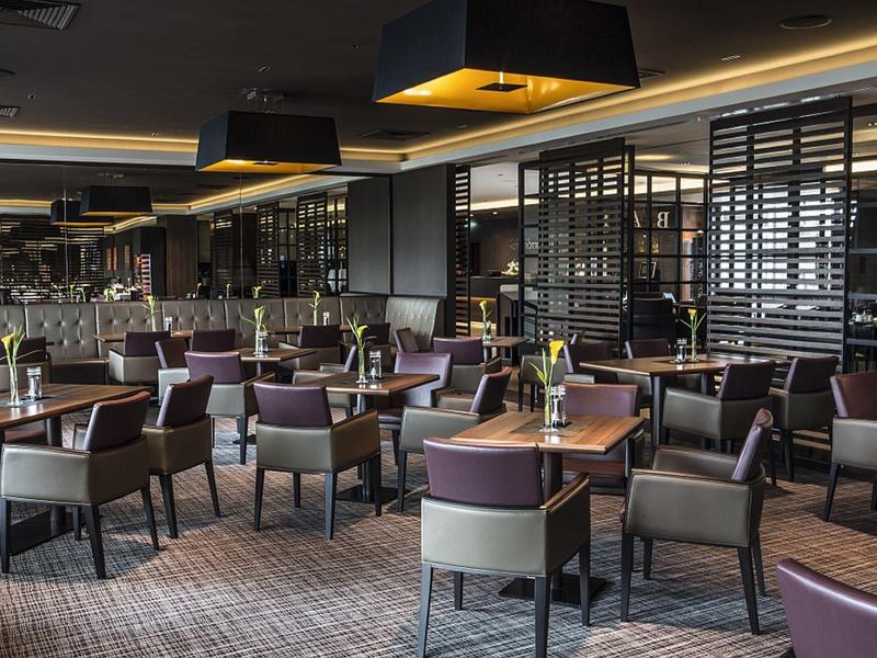 Moderner Gastraum mit dunklen Möbeln, grauem Teppich und warmem Licht an der Decke.