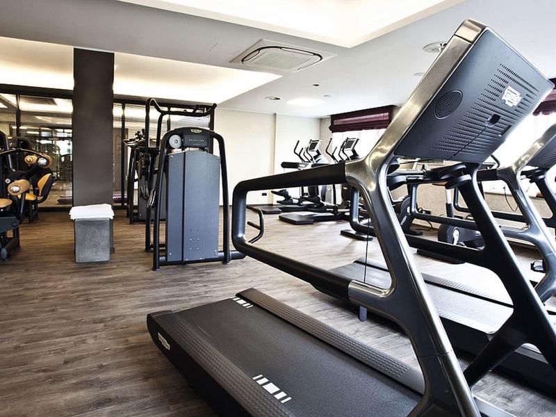 Moderne Fitnessstudio mit Laufbändern, Trainingsmaschinen und hellem Raum mit Holzfußboden.
