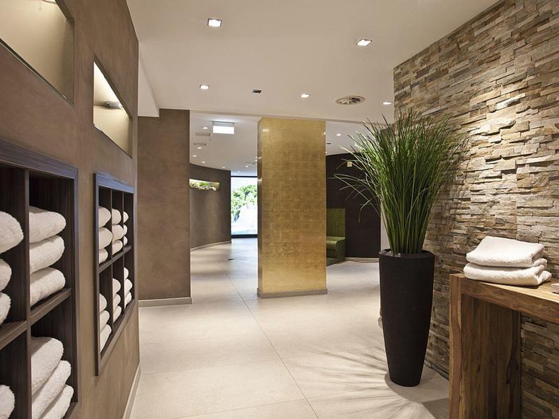 Moderner Flur mit Steinwand, grüner Pflanze und weißen Handtüchern in Nischen und auf Tisch.