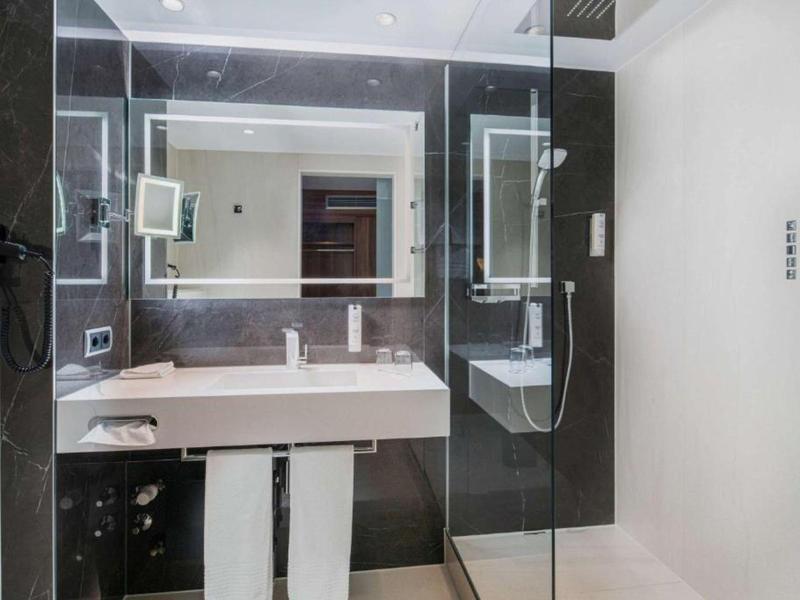 Moderner Badezimmerspiegel mit LED-Beleuchtung, weißem Waschtisch und Glas-Duschabtrennung.