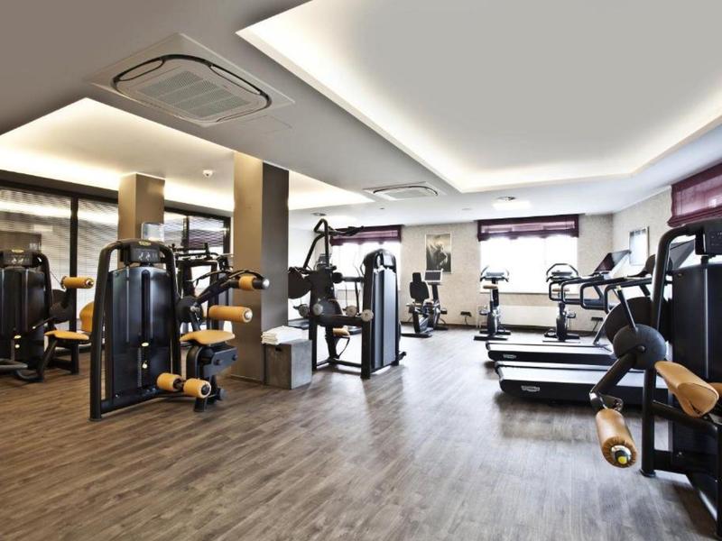 Moderner Fitnessraum mit Geräten, Holzfußboden und großer Fensterfront für Tageslicht.