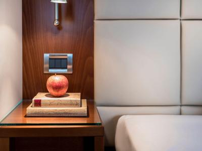 Eleganter Nachttisch mit Holzwand, moderner Lampe und roten Dekorationsapfel neben weißem Bett