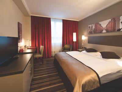 Modernes Hotelzimmer mit großem Bett, Fernseher, rotbraunen Vorhängen und stilvoller Einrichtung.