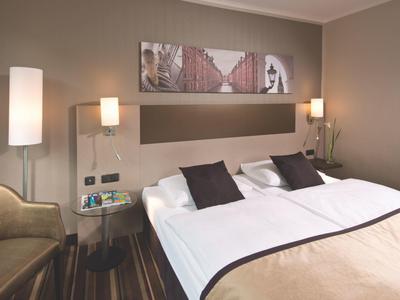 Modernes Hotelzimmer mit großem Bett, zwei Nachttischlampen und einem Sessel in der Ecke