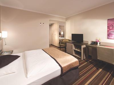 Modern eingerichtetes Hotelzimmer mit Doppelbett, Schreibtisch, TV und warmen Farben.