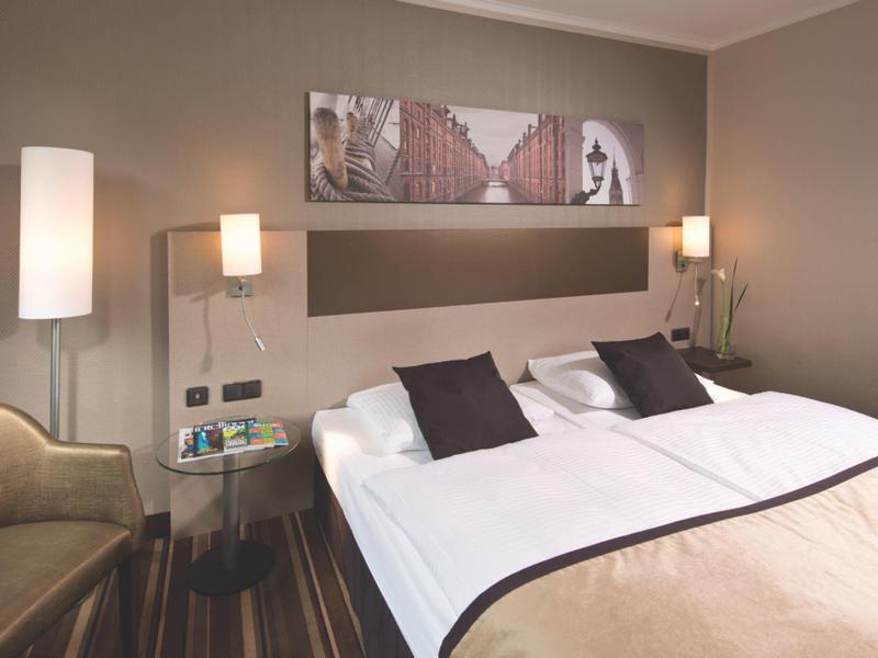 Modernes Hotelzimmer mit großem Bett, zwei Nachttischlampen und einem Sessel in der Ecke