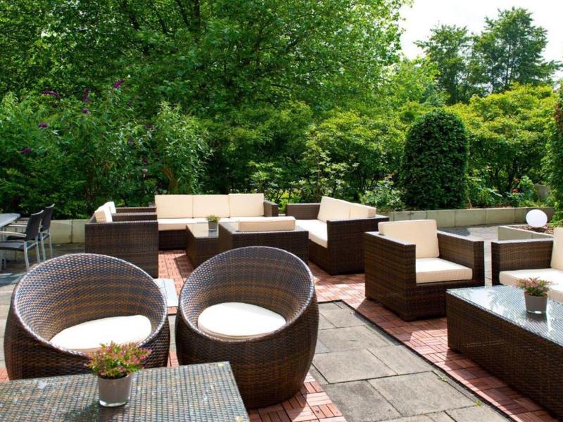 Moderne Hotelterrasse mit braunen Rattanmöbeln und grünen Bäumen im Hintergrund.