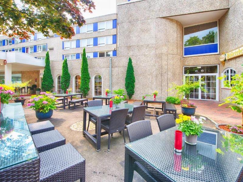 Gemütlicher Außenbereich eines Hotels mit Tischen, Sesseln und Dekoration unter Bäumen.