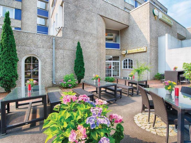 Gemütliche Hotelterrasse mit Blumen, Tischen und Stühlen unter blauem Himmel.