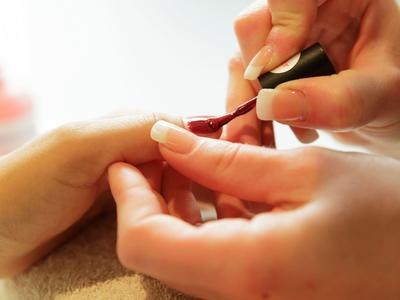 Manikúra nanášející červený lak na nehty.