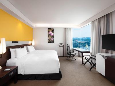 Modernes Hotelzimmer mit großem Bett, gelber Wand, Schreibtisch und Blick auf Stadt und Wasser.