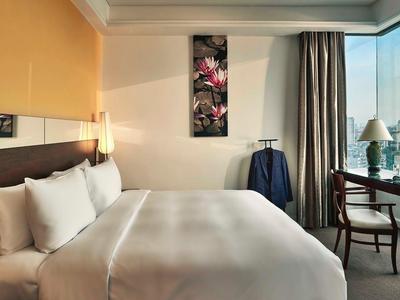 Modernes Hotelzimmer mit großem Bett, Schreibtisch am Fenster und Stadtblick bei Tageslicht.