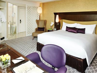 Helles Schlafzimmer mit großem Bett, lila Stühlen, Sesseln und Glastür zum Badezimmer.