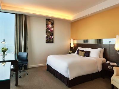 Modernes Hotelzimmer mit Doppelbett, Schreibtisch, Sessel, großer Fensterfront und gelb gestrener Wand.