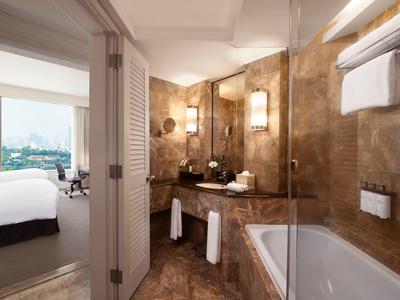 Modernes Badezimmer mit braunen Fliesen, Badewanne, Waschbecken und Blick ins Schlafzimmer.