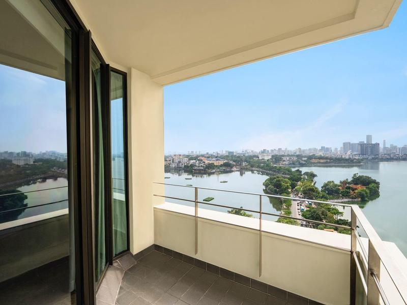 Balkon mit Glasgeländer bietet Blick auf einen Fluss, Stadt und grüne Insel bei klarem Himmel.
