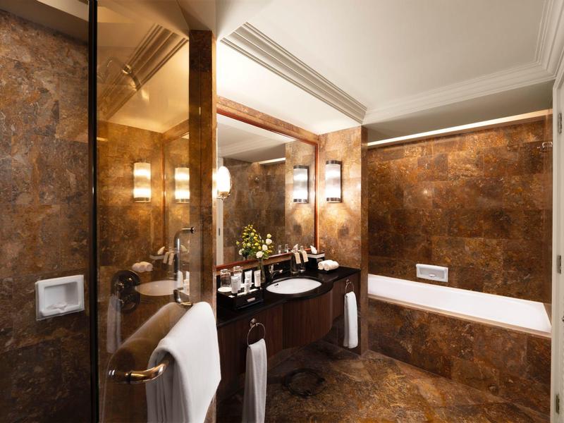 Luxus-Bad mit braunen Marmorfliesen, großer Spiegel, Doppelwaschbecken und Badewanne.