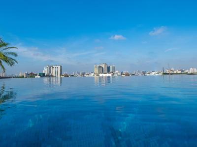 Infinity-Pool mit klarem blauem Wasser, Palmen links, Stadt-Skyline im Hintergrund, blauer Himmel.