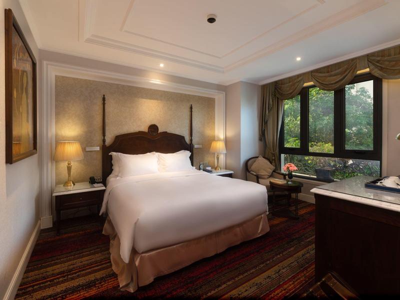 Gezellige hotelkamer met groot bed, tapijt en groot raam met uitzicht op groen.