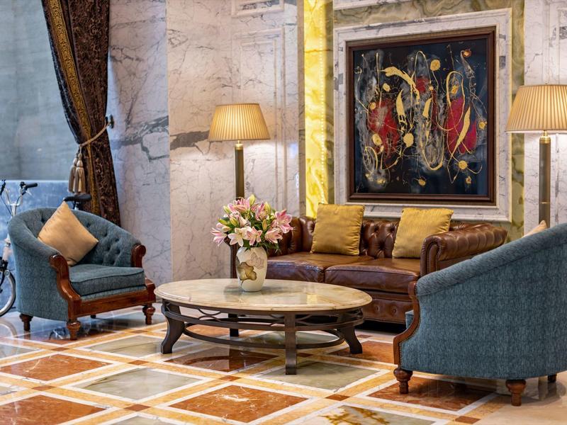 Elegant hotelkamer met leren bank, blauwe fauteuils, marmeren salontafel en kunstwerk aan de muur.