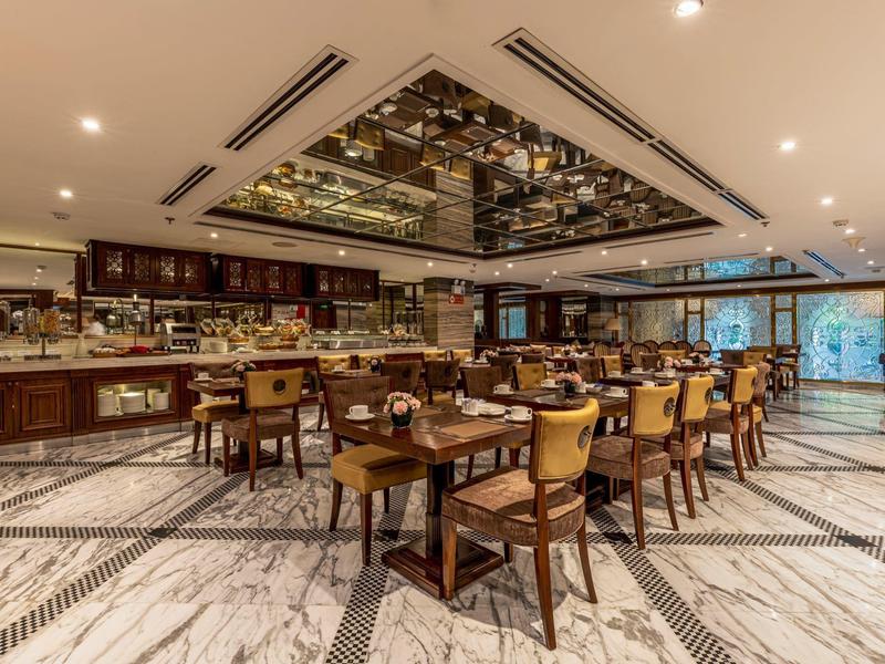 Elegant hotelrestaurant met marmeren vloer, houten meubels en een decoratieve spiegel aan het plafond.