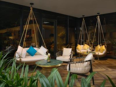 Gemütliche Hängesessel und Sitzgruppe auf einer Hotelterrasse mit Pflanzen und Glaswand.