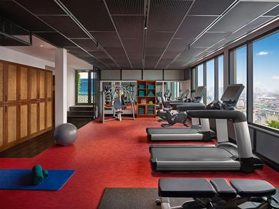 Fitnessraum mit Laufbändern, Hanteln und großen Fenstern mit Blick auf die Stadt.