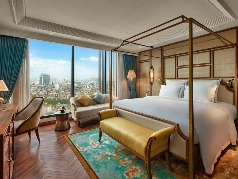 Chambre d'hôtel luxueuse avec lit à baldaquin, coin salon et grande fenêtre avec vue sur la ville.