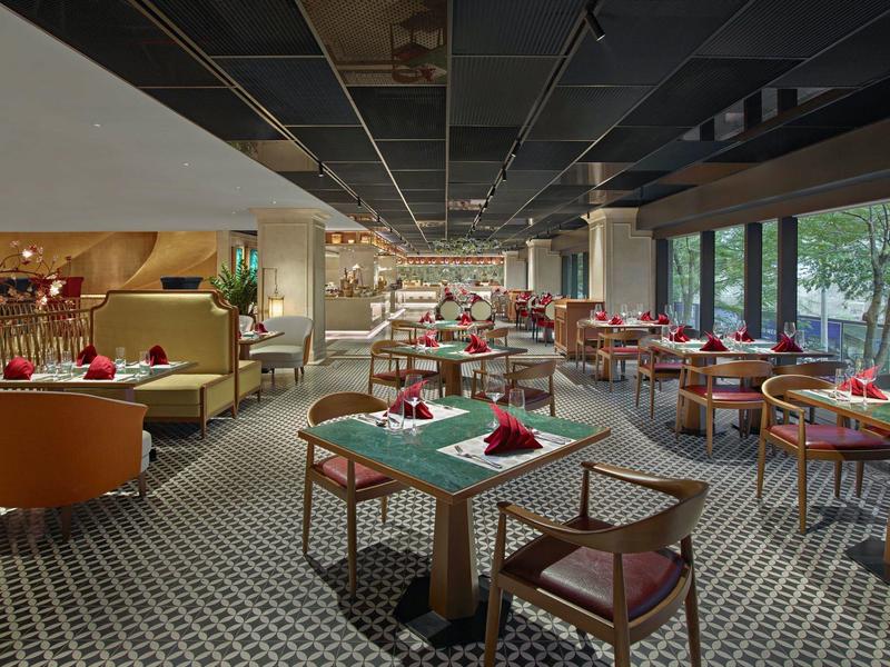 Salle à manger moderne avec tables, chaises et grandes fenêtres donnant sur la verdure.