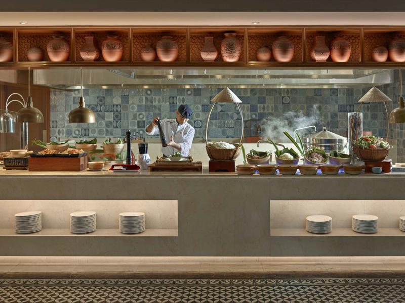 Cuisine d'hôtel moderne avec chef et buffet approvisionné sous lumière chaude.