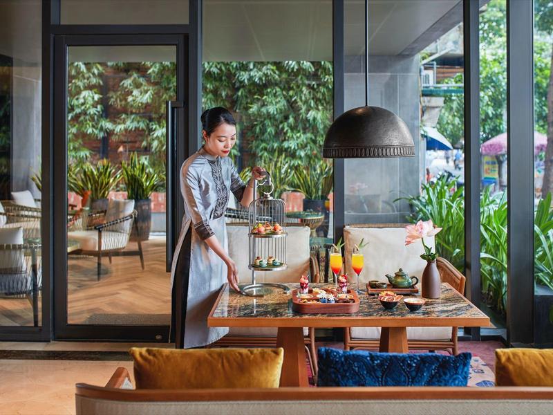Une femme prépare une table sur la terrasse d'un restaurant avec vue sur des plantes vertes.
