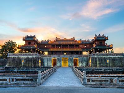Historisches asiatisches Schloss bei Sonnenuntergang mit symmetrischem Steinweg und blauem Himmel.