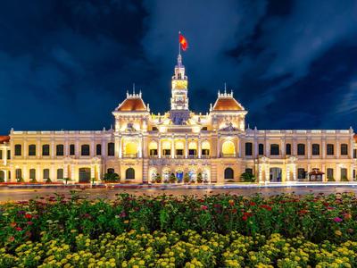 Beleuchtetes historisches Gebäude bei Nacht mit Blumenbeet im Vordergrund.