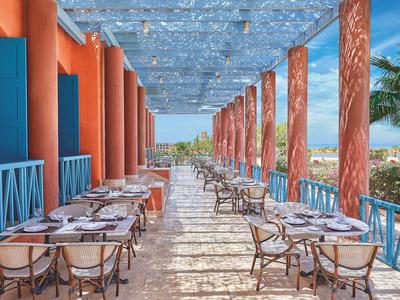 Area pranzo all'aperto con tavoli e sedie sotto una tettoia blu vicino al mare.