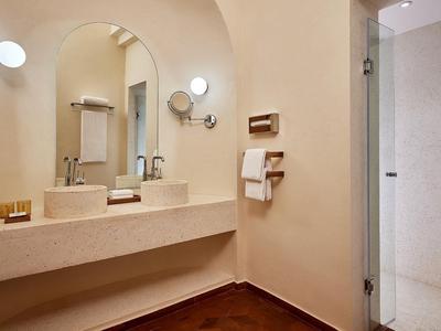 Bagno moderno in hotel con pareti beige, grande specchio, doppio lavabo e doccia a filo pavimento.
