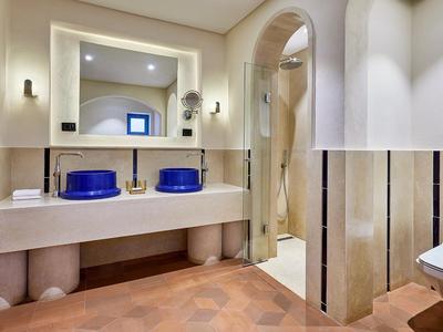 Bagno moderno in hotel con doppi lavandini blu, grande specchio e piastrelle beige.