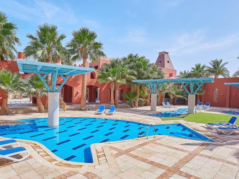 Piscina esterna con acqua blu, circondata da lettini e palme sotto un cielo limpido.