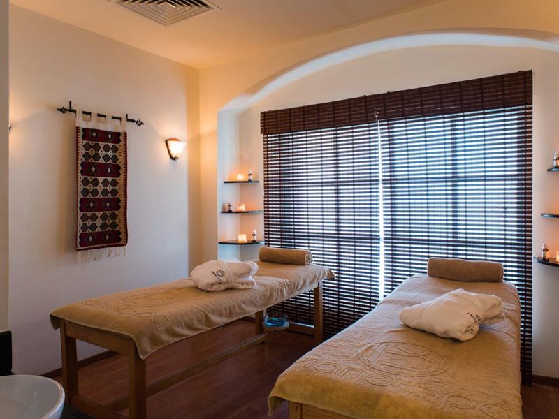 Accogliente stanza spa con due lettini da massaggio, illuminazione soffusa e grandi tende alla finestra.