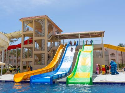 Colorful water slides lead into a hotel pool alongside a water playground on a sunny day.