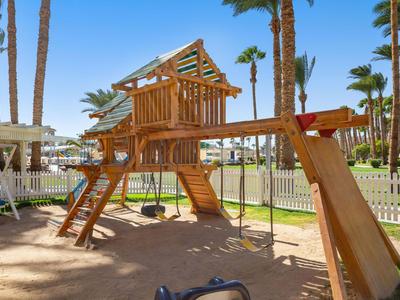 Children's playground with wooden structure, slide, and swings in sunny outdoor area.