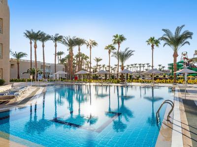 Clear swimming pool with palm trees and sun loungers under a blue sky at a hotel resort.