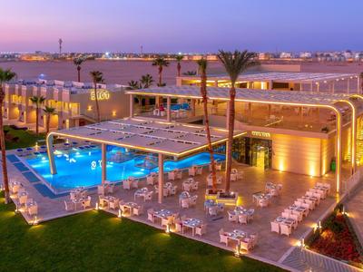 Evening view of a modern hotel with illuminated pool and outdoor dining area in a coastal setting.