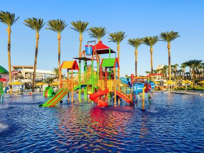 Colorful water playground structure in a pool with palm trees in the background under a clear sky.