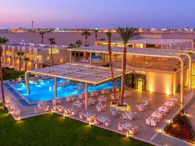 Modern hotel with illuminated pool and outdoor dining area at sunset.