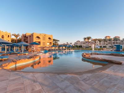 Grand piscine extérieure devant un hôtel avec parasols et ciel bleu clair.