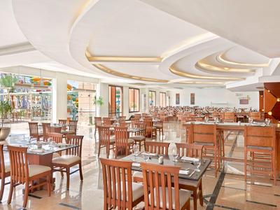 Restaurant lumineux et moderne avec tables et chaises en bois, grandes fenêtres et plafond décoratif.