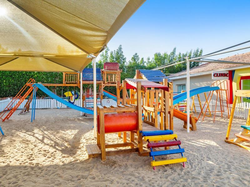 Bunter Kinderspielplatz mit Klettergeräten, Rutschen und Sandfläche unter Sonnensegel.