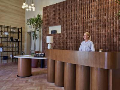 Nowoczesna drewniana recepcja hotelowa z zakrzywionym biurkiem i stojącą pracownicą.