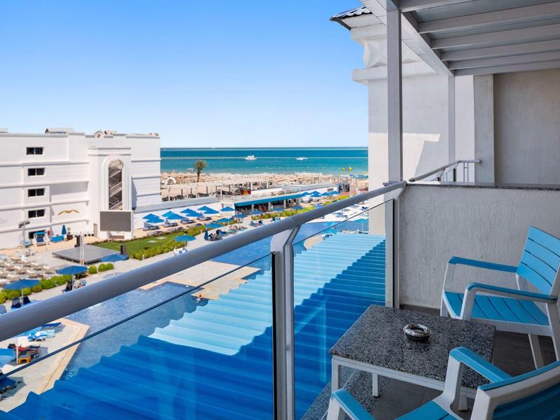 Balcone dell'hotel con sedie blu che si affaccia sul mare e sul parcheggio con cielo sereno.