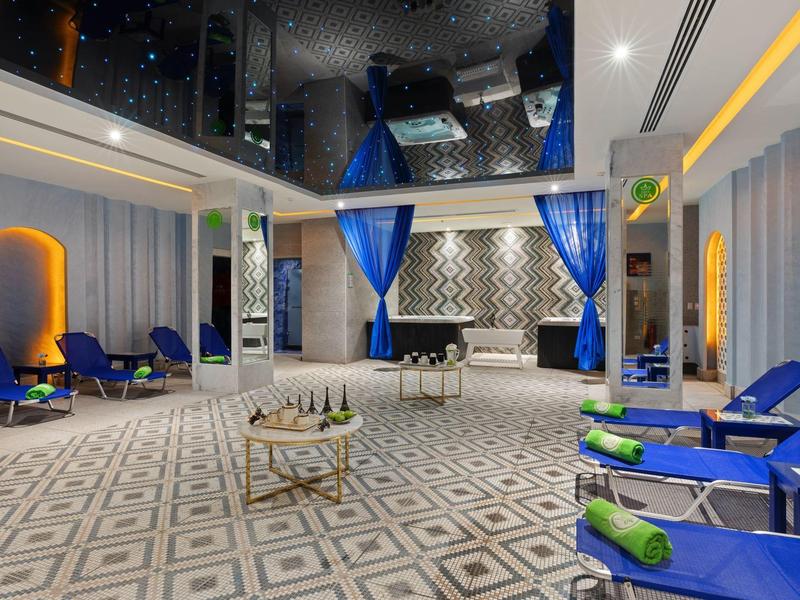 Lounge d'hotel elegante con poltrone blu, tende e interni moderni illuminati.